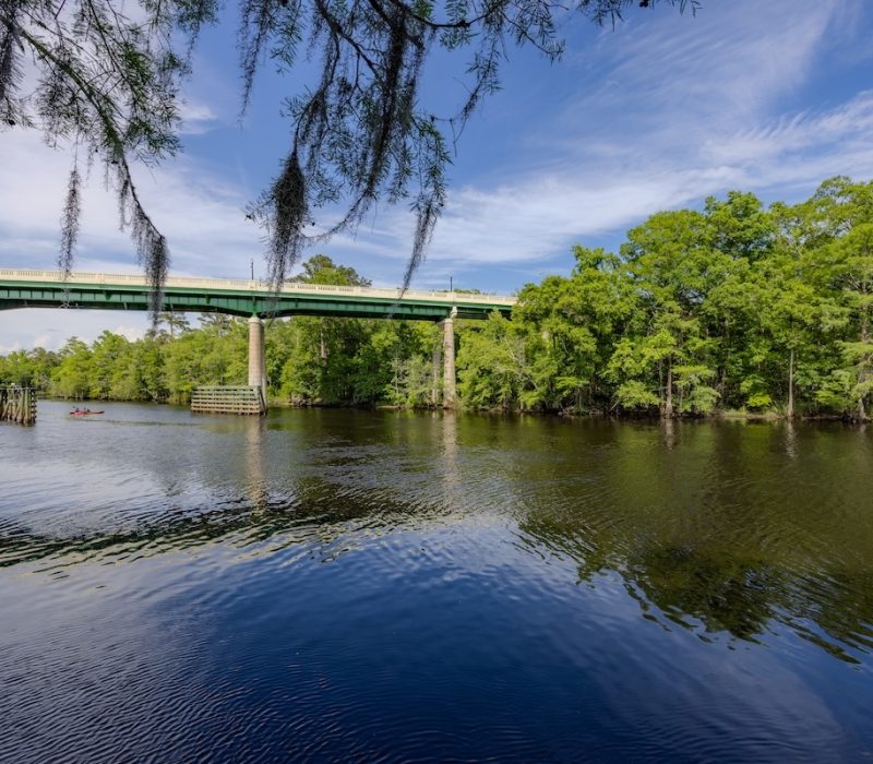 A serene view by the Conway Riverwalk of Waccamaw River and Waccamaw River Memorial Bridge with a kayak passing underneath it, at Conway, South Carolina. HDR encoded